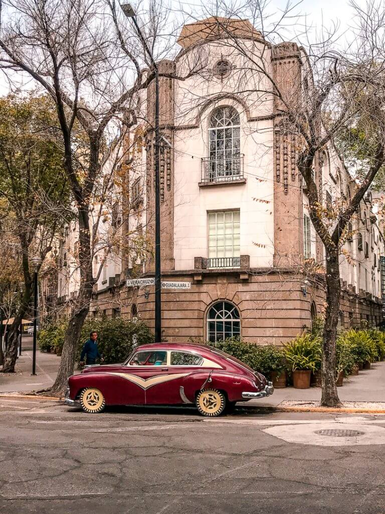 a maroon vintage car sits in front of an art deco building on the corner of Calle Veracruz and Calle Guadalajara in Mexico City's La Condesa neighborhood