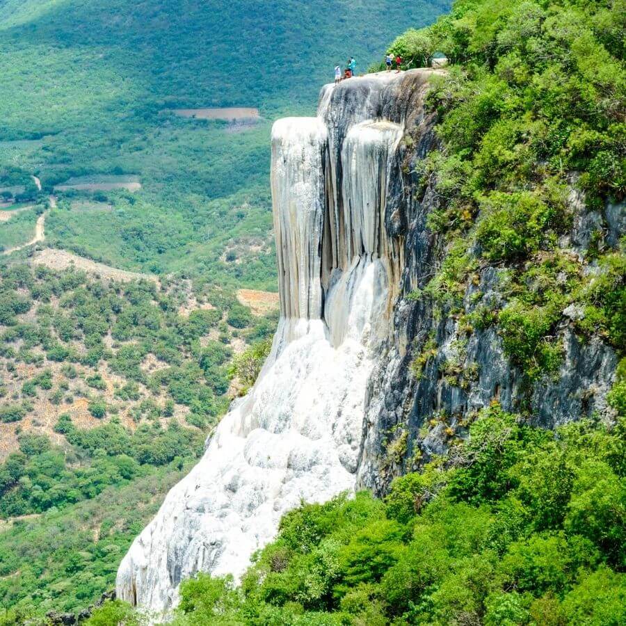 a long-range view of Hierve el Agua, Oaxaca, with calcified water pouring down the cliff above a green valley