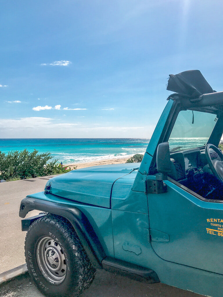 looking over the hood of a blue jeep at the turquoise Caribbean sea and Cozumel beaches
