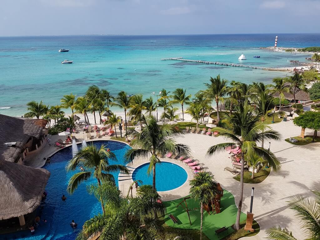 aerial view of an all-inclusive resort in mexico with multiple pools surrounded by palm trees and the caribbean sea in the background