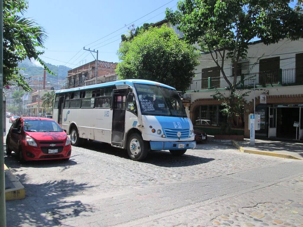 a blue and white bus rolls along a cobblestone street in Puerto Vallarta, Mexico