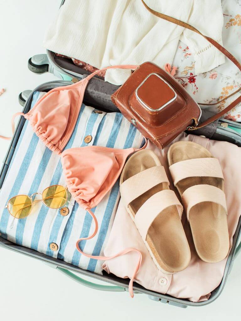 flat lay image of a suitcase packed with women's beach clothing and accessories