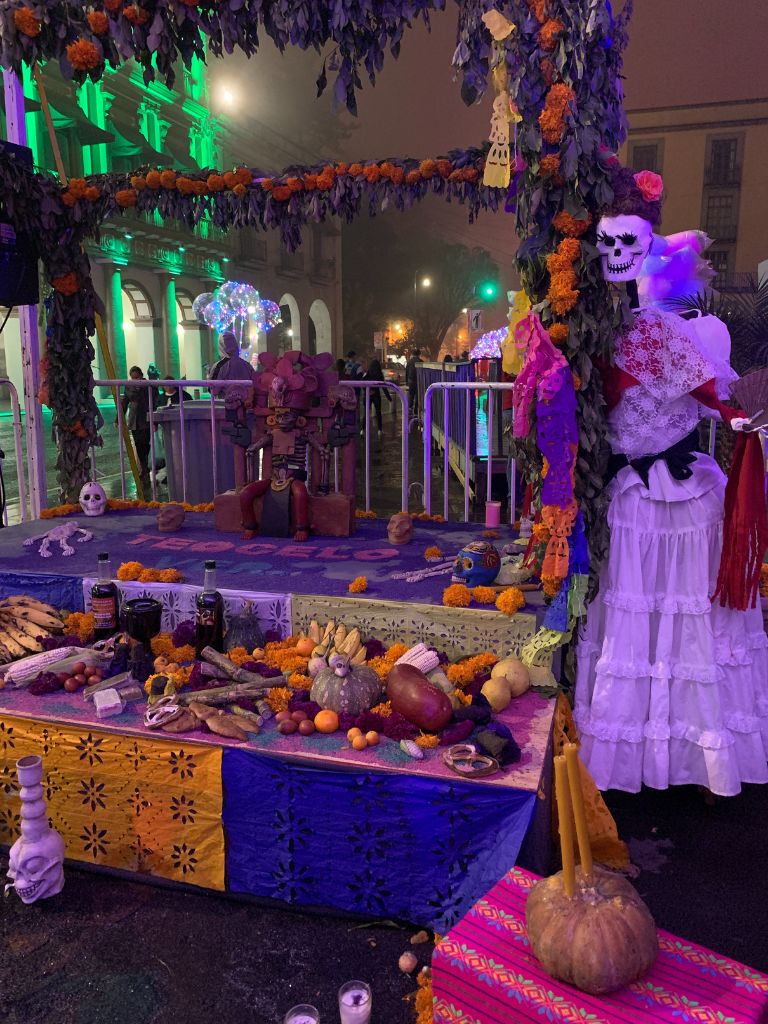 Day of the Dead altar in Xalapa, Veracruz featuring gourds, marigolds, bananas, pottery, and a catrina sculpture. 