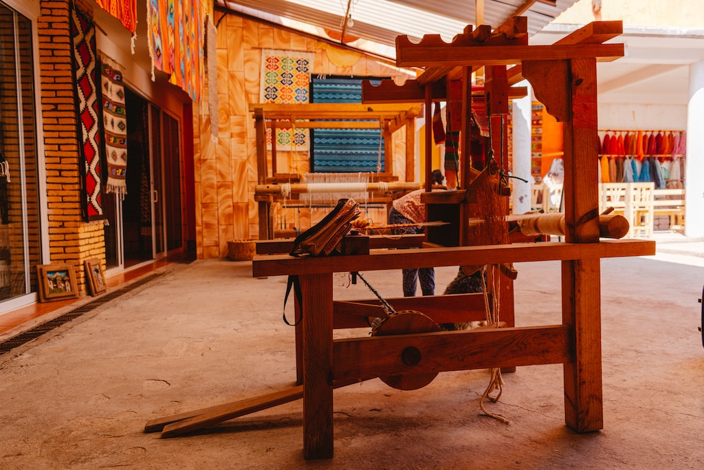 Traditional Oaxacan textile shop displaying colorful fabrics and a wooden weaving loom, exemplifying the local craftsmanship you'll find in Oaxaca.