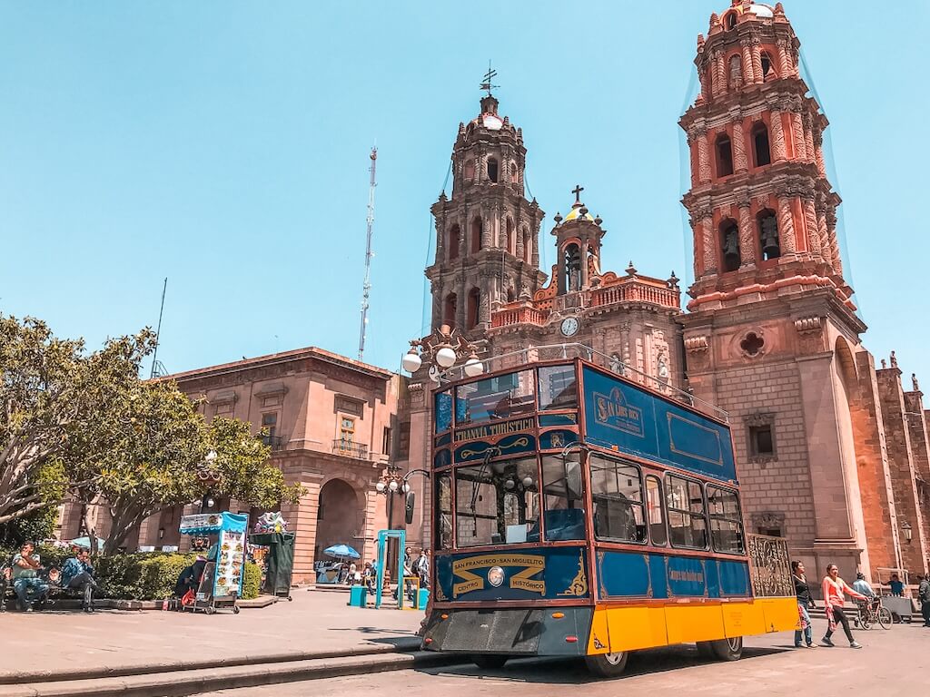 street-car style tourist tram is parked in front of a pink stone church on a plaza in San Luis Potosí, central Mexico