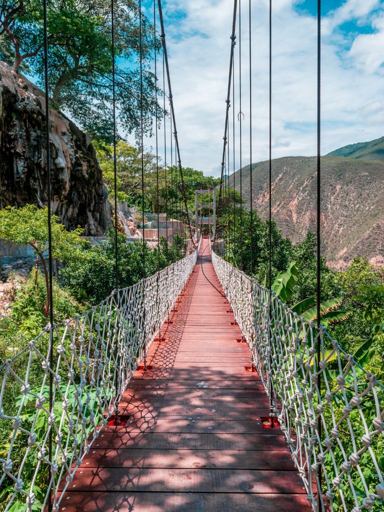 looking across the Tolantongo suspension bridge to the hot springs pools on the other side. lush greenery is visible on either side