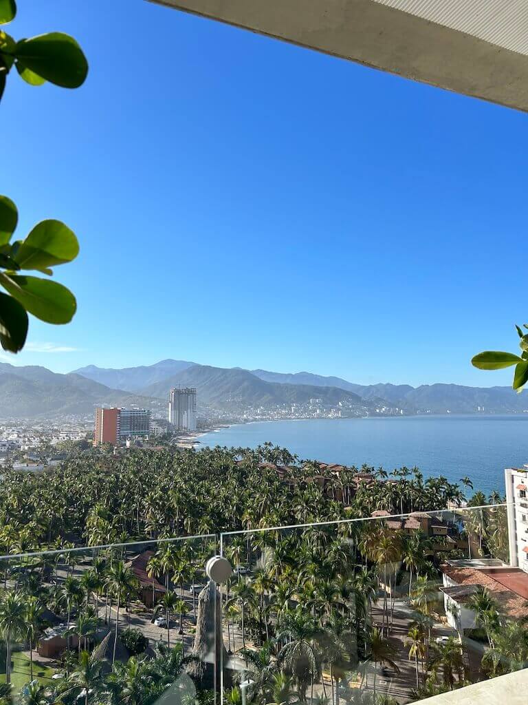 Looking south along Puerto Vallarta's coastline from a high balcony. Tall hotel buildings line the shoreline in the distance.