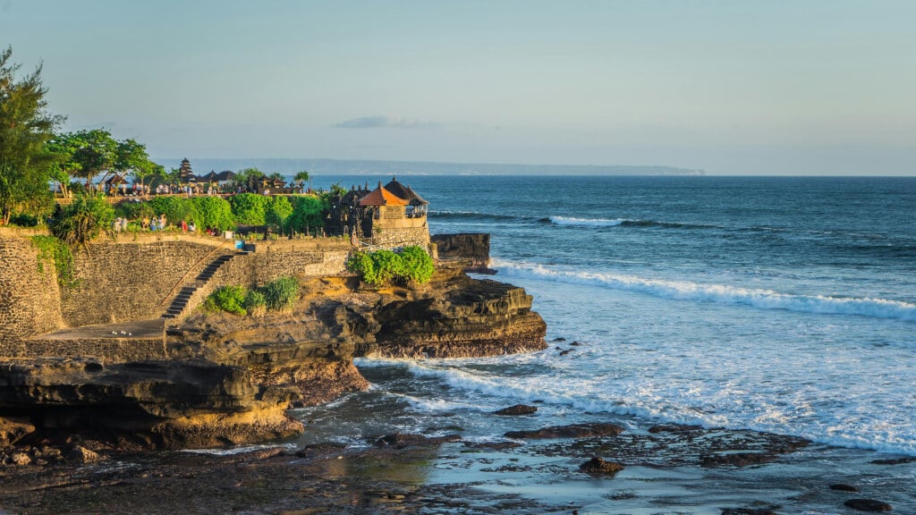 Aerial view of tanah lot temple in bali, surrounded by beautiful rocky shores and ocean waves.