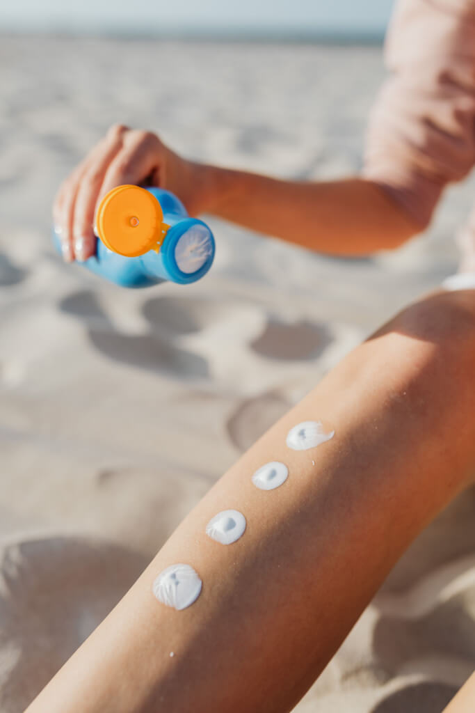 Biodegradable sunscreen lotion on leg at the beach. Summer skincare routine for sun protection outdoors.